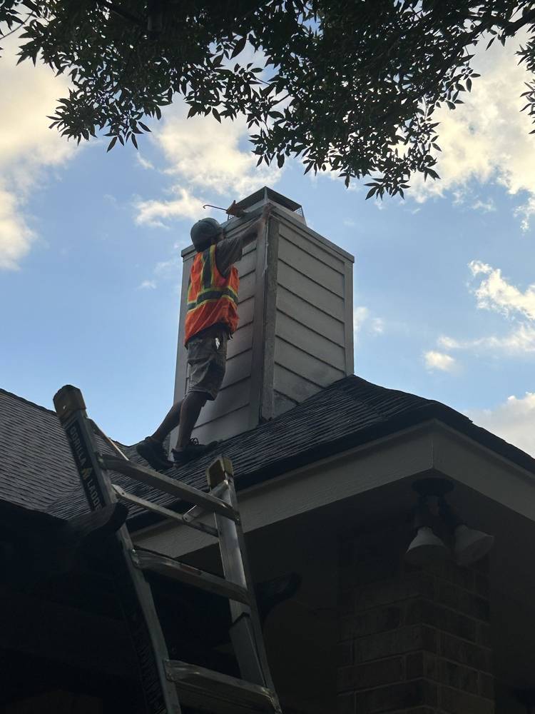 Crew member repairing chimney siding and flashing from the roofline