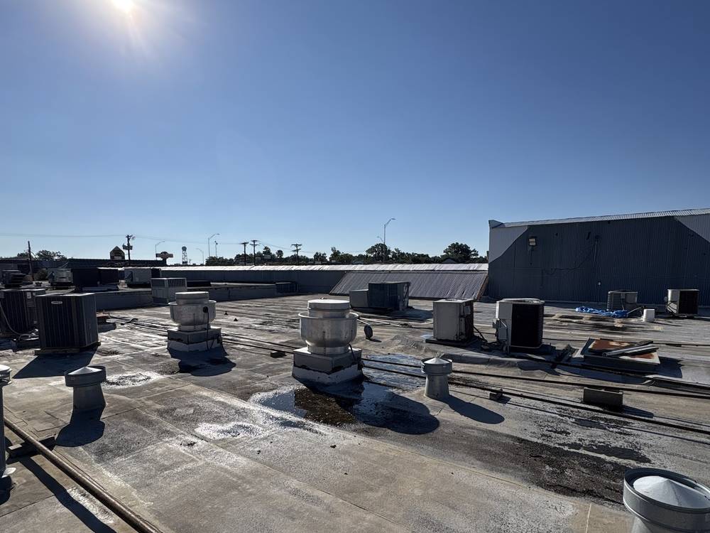 Commercial flat roof with rooftop units and vents under a bright, clear sky
