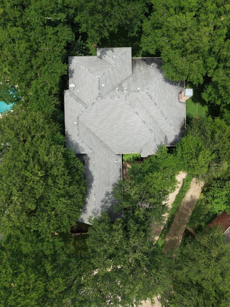 Top-down drone view of a gray shingle roof surrounded by tree canopy