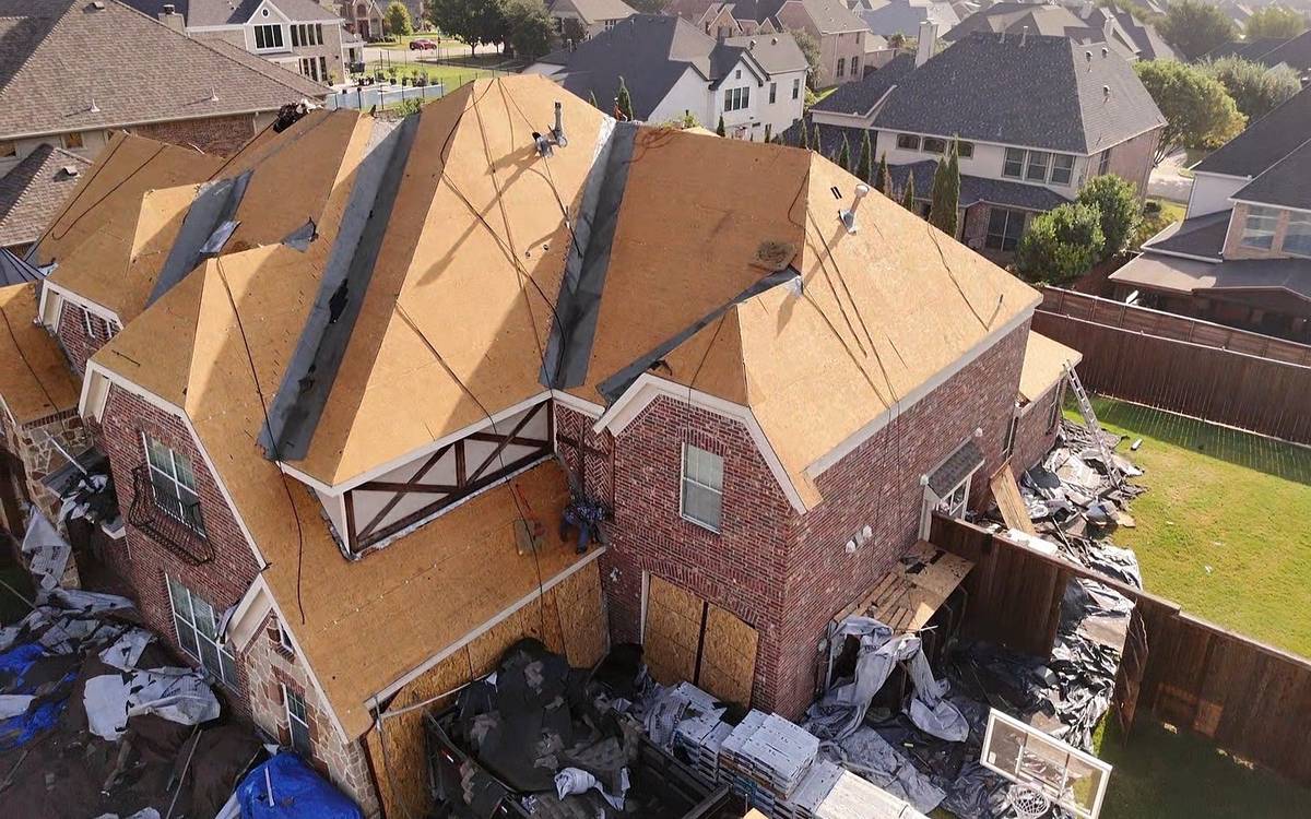 The same brick home in July 2026, old roof torn off and new roof decking installed