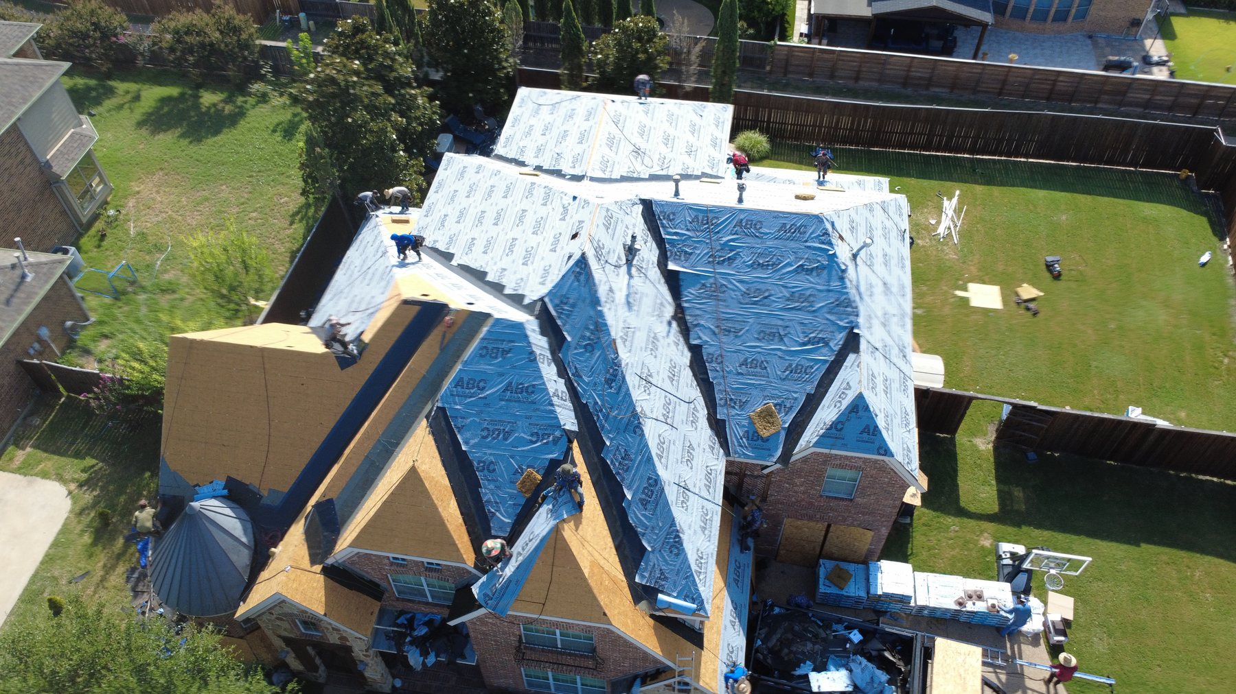 Roof tear-off in progress with debris tarped and staged