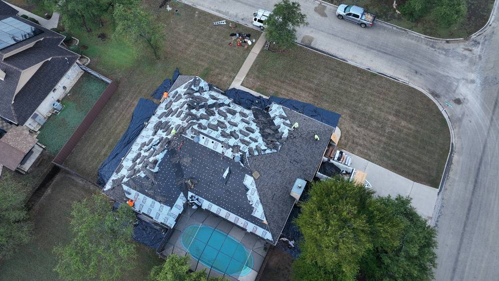 Our crew tearing off an old shingle roof on a corner-lot home with a backyard pool, drone view