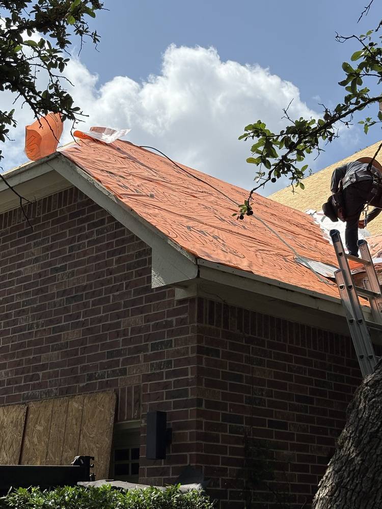 Roofer in a fall-protection harness laying synthetic underlayment on a brick home