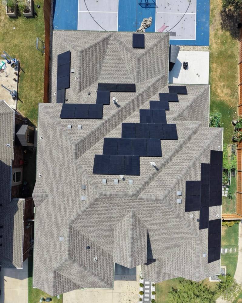 Top-down drone view of a gray shingle roof with rooftop solar panels