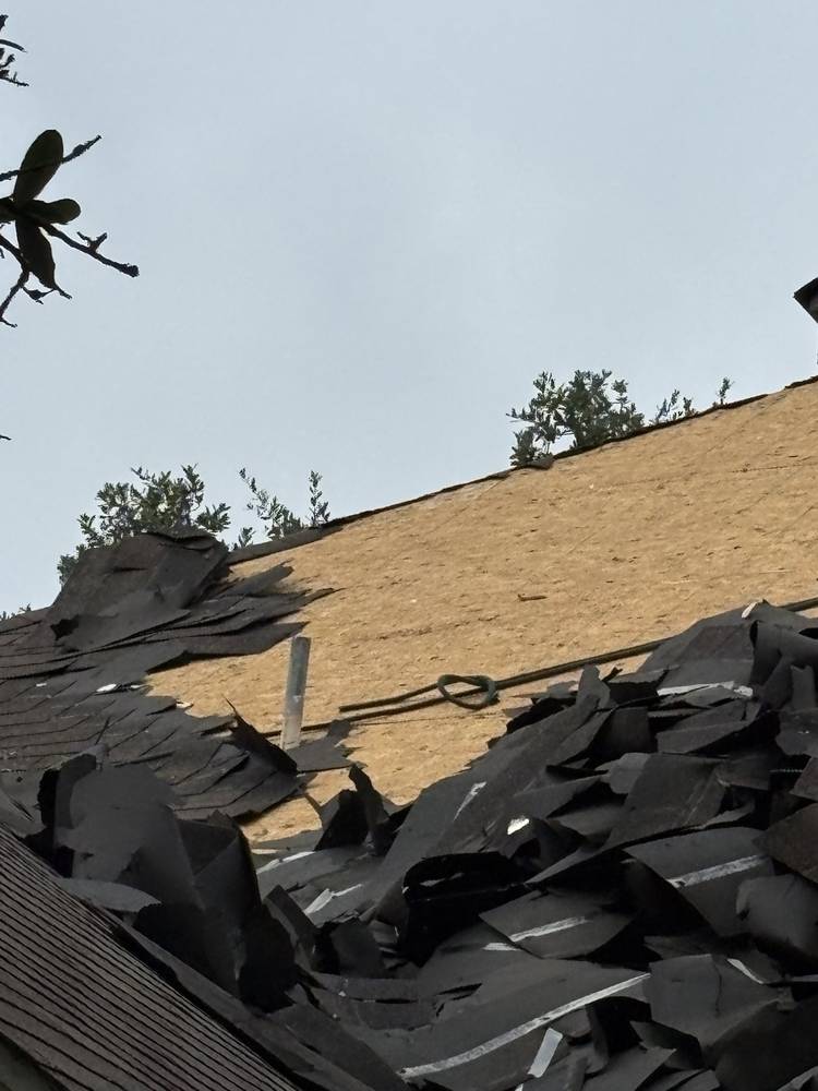 Torn-off shingles piled on bare decking during a storm tear-off
