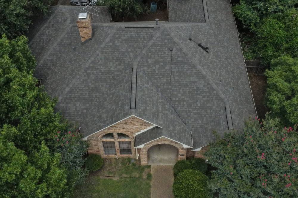 Weathered gray shingle roof on a brick home with a chimney, aerial inspection view